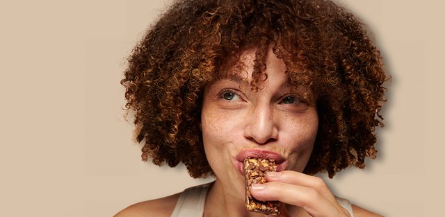 Person enjoying a granola bar against a beige background.